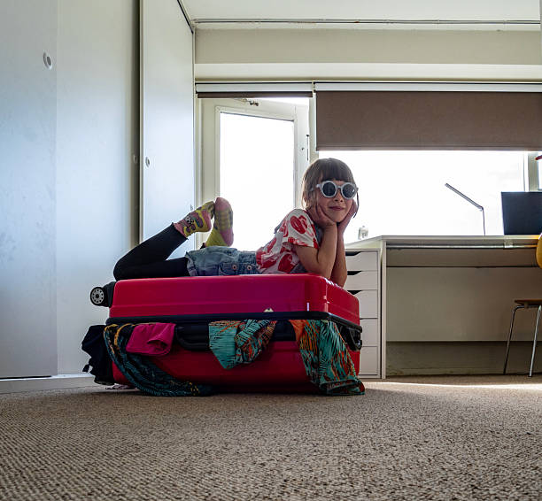 Real moments of family packing their suitcases and bags in their homes to prepare for an upcoming trip. Daughter  trying to fit everything in the suitcase, and ready for vacation.