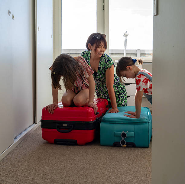 Real moments of family packing their suitcases and bags in their homes to prepare for an upcoming trip. Daughter  trying to fit everything in the suitcase, mother helping.