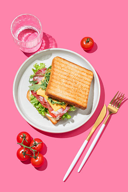 istock Toast bread sandwich with bacon, cheese, tomatoes, lettuce, arugula and sauce on a plate on a pink background 2226261595