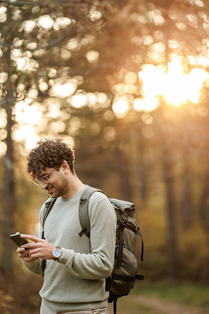 istock Handsome young man using mobile phone while hiking in sunny autumn woods 2226261715