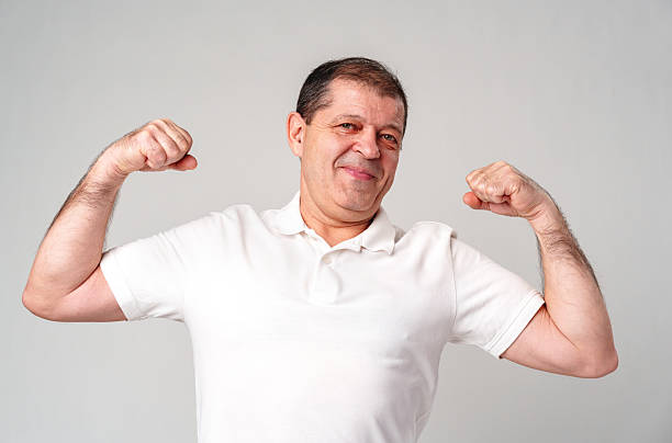istock Happy older man showing off his strong biceps while standing against a light gray background 2226262097