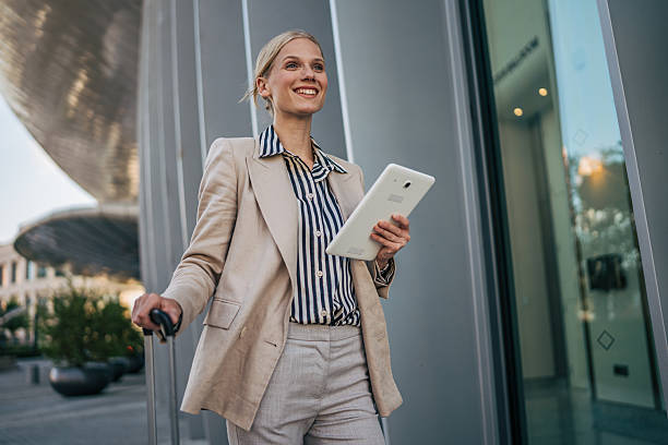 istock Businesswoman walking with suitcase and using digital tablet outside office building 2226262899