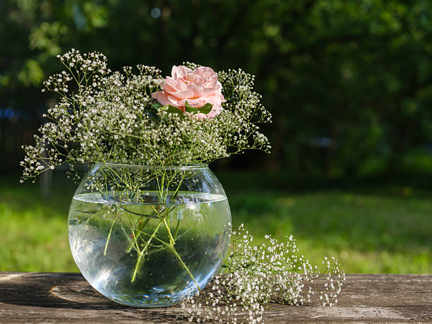 round glass vase with white flowers and rose on wooden table in summer garden