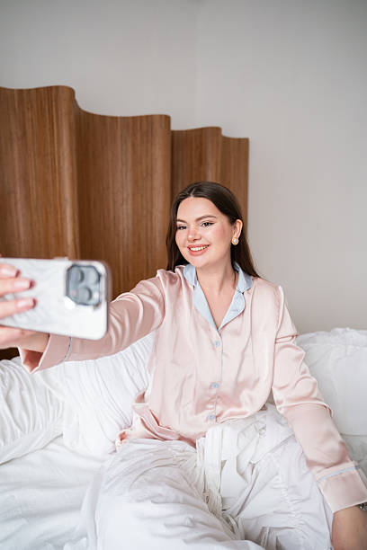 istock Woman taking a selfie while sitting on bed in satin pajamas 2226266451