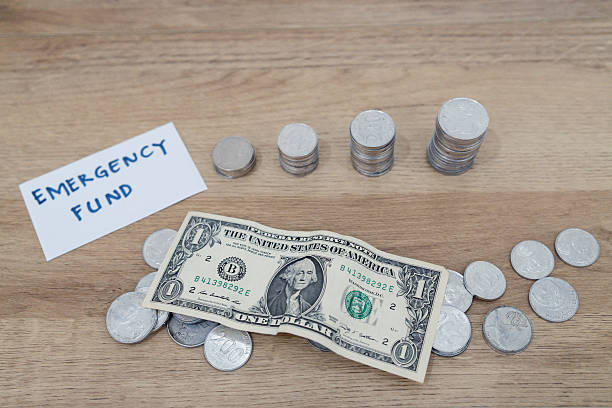 istock Clear jar marked emergency fund with stacked coins, folded dollar bills, and loose change on wooden table. 2226266802