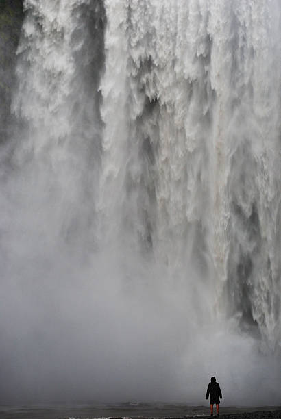 A breathtaking view of a powerful Icelandic waterfall cascading with immense force. A lone figure stands in the foreground, emphasizing the grandeur and scale of nature. This awe-inspiring scene evokes feelings of wonder, serenity, and the raw beauty of untouched landscapes