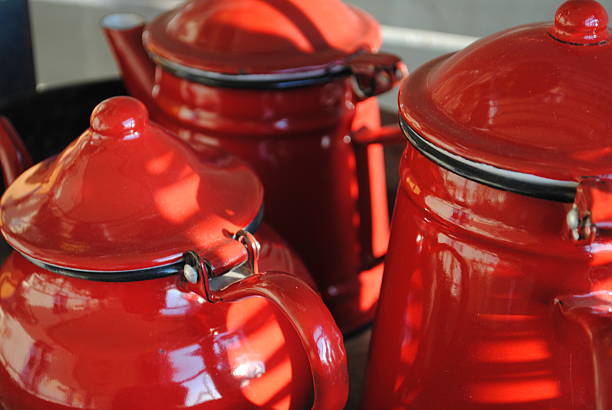 A collection of vintage red enamelware pots and a matching mug on a neutral surface, evoking a sense of cozy, rustic kitchen life and nostalgic charm
