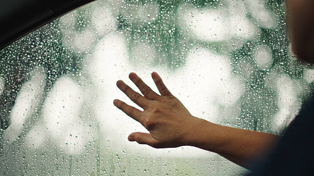 Close-up hand connecting with nature through rainy car window in peaceful moment.