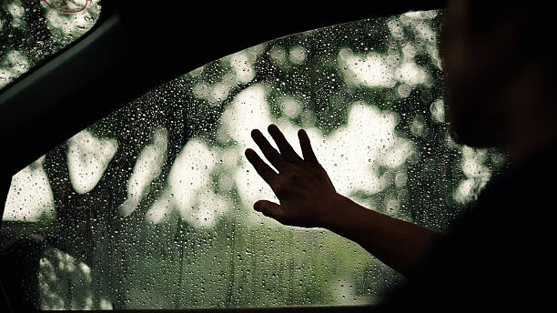 Silhouette of hand touching rainy car window from inside.