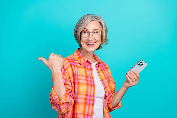 istock Happy elderly woman holding smartphone and gesturing with a smiling expression against a teal background 2226272078