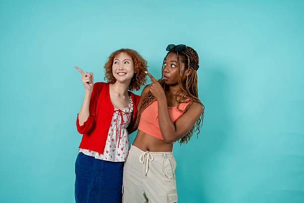istock Two young Diverse Generation Z women posing on isolated blue screen. Attractive different stylish girls smile and looking at camera showcasing friendship, fun, and youthful energy in studio together. 2226272117