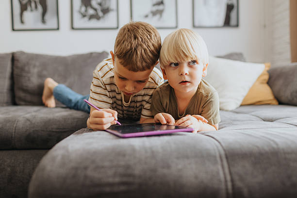 istock Cute blond brothers using digital tablet while lying on sofa together at home 2226275185