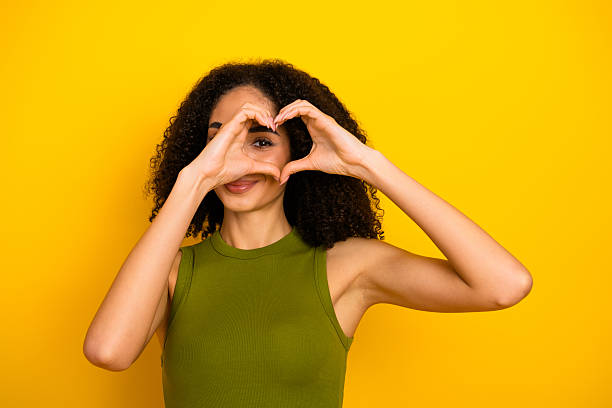 istock Charming young woman making a heart shape with her hands while smiling against a vibrant yellow background 2226276385