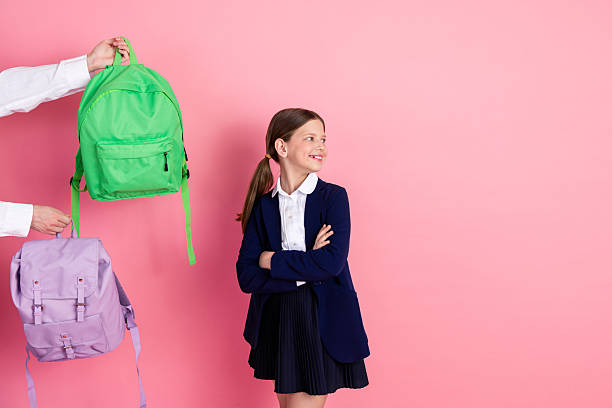 istock Charming schoolgirl with ponytails considering options between colorful backpacks in preparation for school on pink background 2226278515