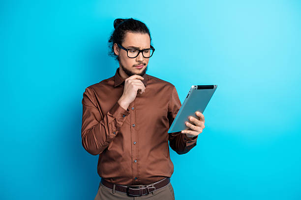istock Young professional man holding a tablet with a contemplative expression, dressed in elegant brown shirt and glasses 2226280022