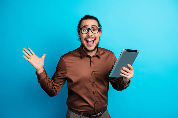 istock Enthusiastic young man holding digital device against teal backdrop, expressing excitement and joy with positive energy 2226280023
