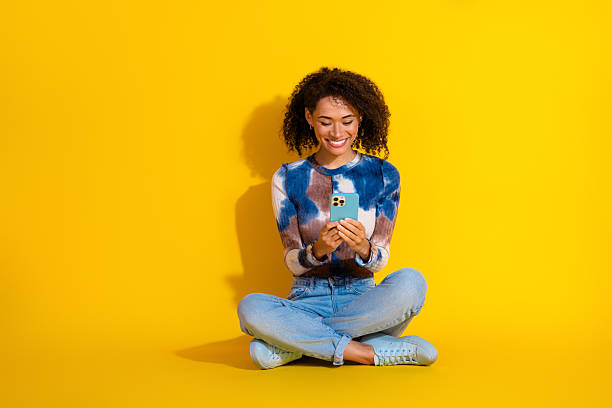istock Young woman using smartphone on vibrant yellow background, smiling joyfully and embracing casual and stylish fashion 2226283529