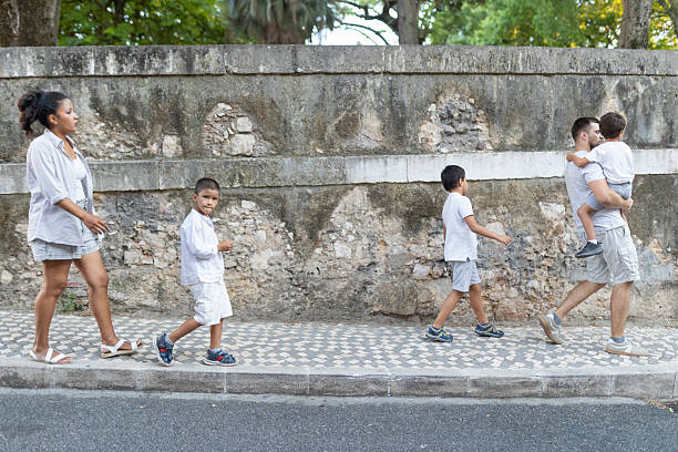 Family with three children taking a walk on sidewalk next to old stone wall