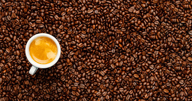 Top view wide banner of espresso in a white cup elevated over blurred roasted coffee beans, with copy space – perfect for coffee ads and branding