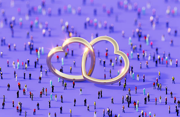 Heart shaped gold colored rings surrounded by human crowd on purple background. Horizontal composition with copy space.