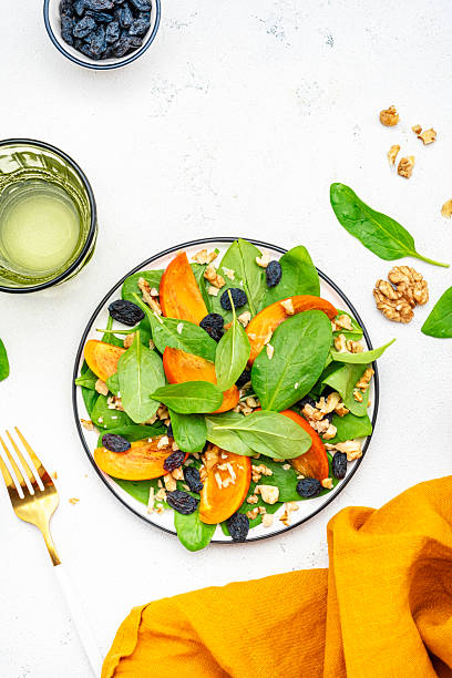 istock Autumn vegan salad with fresh persimmon, walnuts, raisin and spinach, white background, top view 2226296937