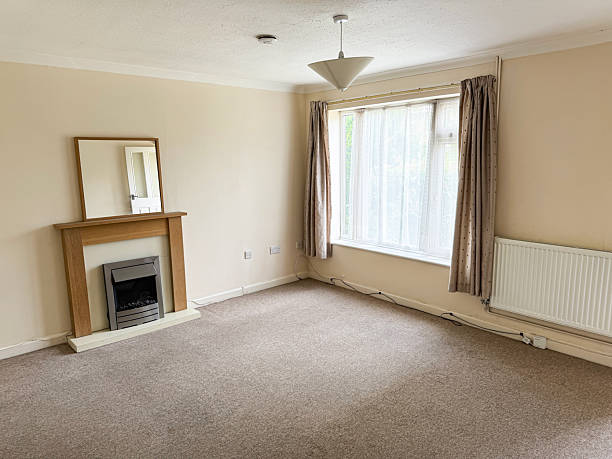 Image of unfurnished lounge featuring brown loop carpet, neutral tones, classic wooden fireplace mantel, decorative wall mirror stock photo