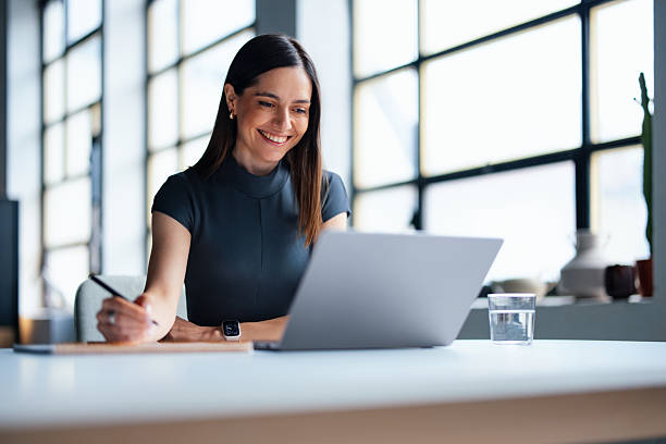 Professional Woman Smiling While Working on a Laptop in a Modern Office