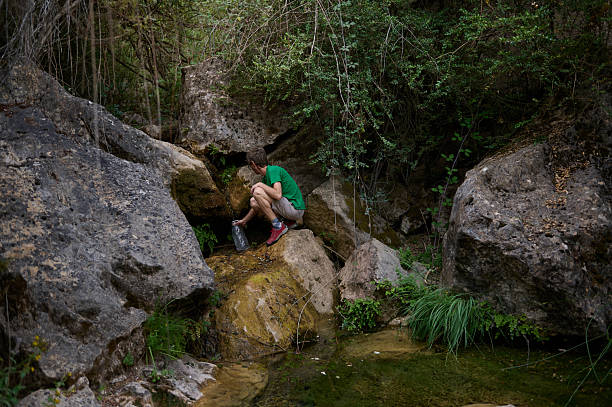 istock Man Refilling Water Bottle at Natural Stream Surrounded by Rugged Rocks 2226307458