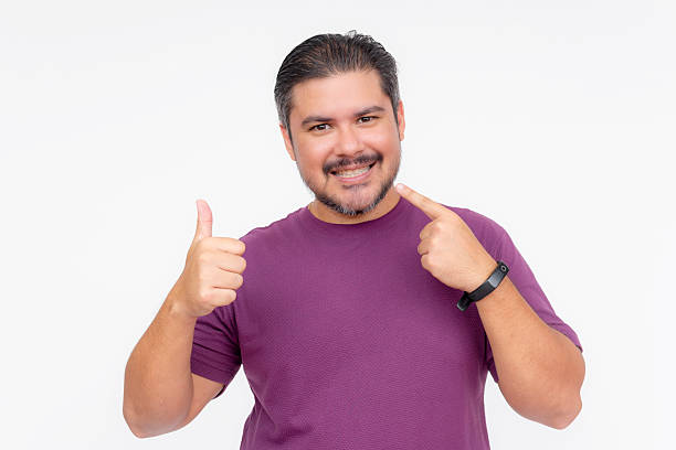 istock A handsome middle aged man pointing to his teeth and smiling while making a thumbs up sign. Dental concept. Wearing a purple waffle shirt. Isolated on a white background. 2226314795