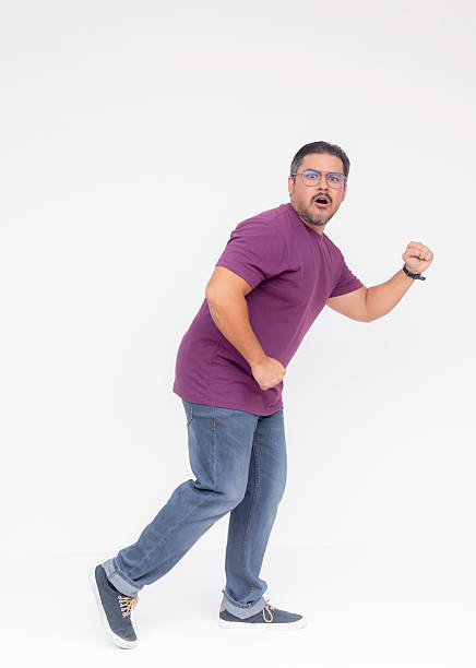 A sneaky middle aged bearded man looking surprised after being caught while walking to the right. Wearing a purple waffle shirt and jeans. Full body photo, isolated on a white background.