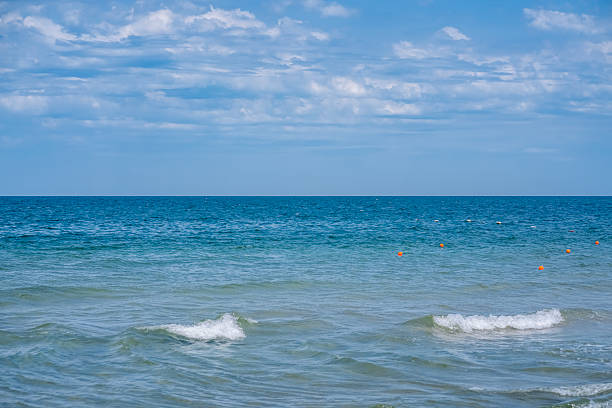 Waves gently lap at the shore while a bright blue sky blankets the summer sea, inviting relaxation and calm. Background.