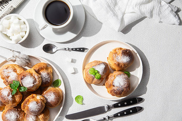Appetizing profiteroles with custard in a white plate on the table. Eclairs, coffee, dessert.