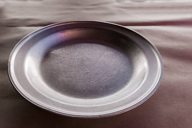 Empty old wide shallow metal aluminum plate on table covered with kraft paper tablecloth, selective focus
