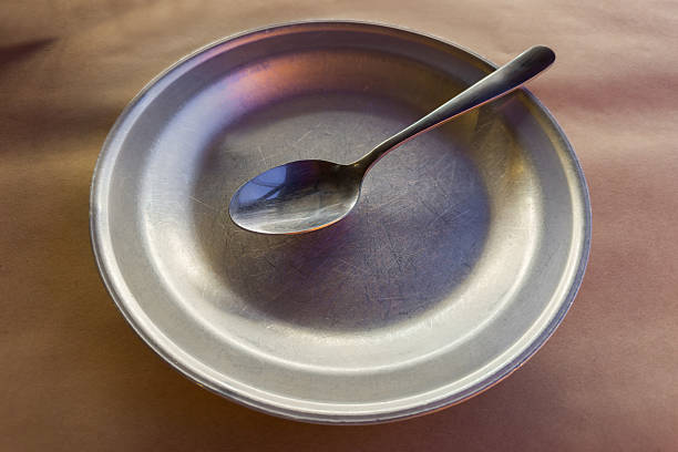 Empty old wide shallow metal aluminum plate with stainless steel spoon on table covered with kraft paper tablecloth