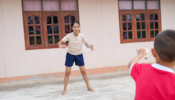 A young girl playing badminton outdoors, focused and ready to hit shuttlecock. scene captures moment of fun and friendly competition in casual setting
