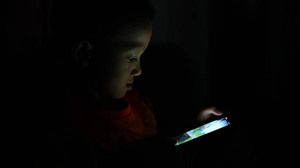 istock Child is focused on smartphone screen in dimly lit environment, showcasing curiosity and engagement. soft glow from device highlights child features, creating serene atmosphere 2226330660