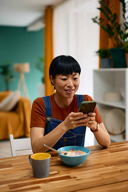 Woman enjoying breakfast and using smartphone at dining table