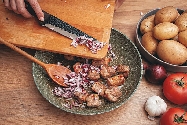 Adding chopped onion to the pan with meat, close-up.