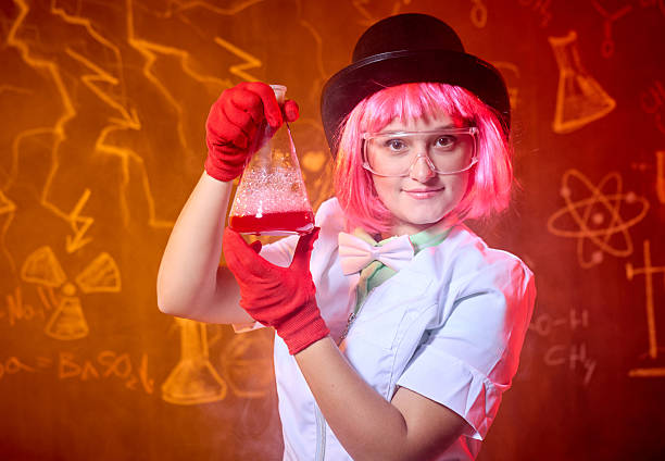 Amusing science, cheerful entertainment at a children's party. Funny young woman dressed in a white lab coat, protective glasses and gloves. Crazy female chemist is doing chemical experiments and making funny face. Studio shooting on background with the chalk drawing on blackboard on chemical theme