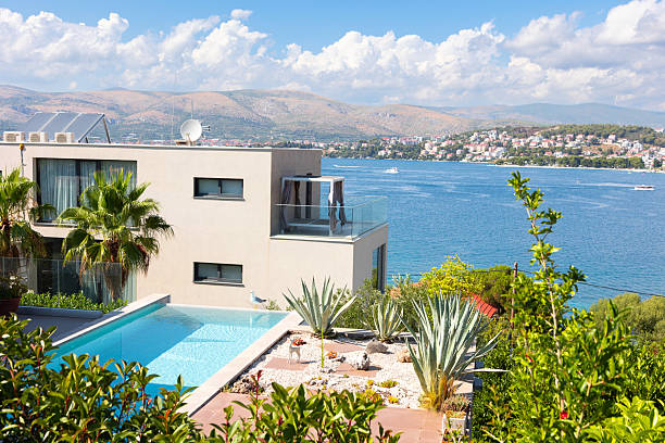 Wide angle shot of a small, all-inclusive  hotel in the Mediterranean countryside,  spacious terrace with sun beds and a swimming pool attached to the house. Blue sky and bright daylight.