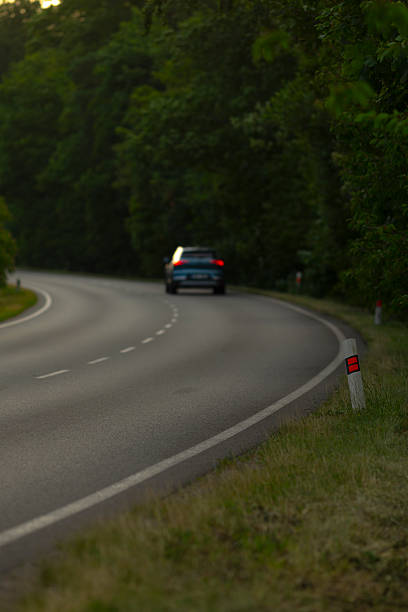 istock A car drives steadily down a winding road surrounded by tall trees 2226350089