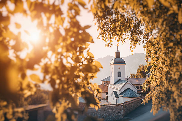 istock Warm sunlight shining through colorful autumn leaves on a white orthodox Serbian monastery Sretenje in a mountain valley of Ovcar Kablar 2226356504