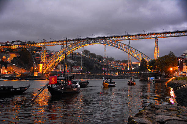 Porto, Portugal - October 11, 2024: Typical boats at the Porto dock at sunset, with the Dom Luis bridge illuminated at background.