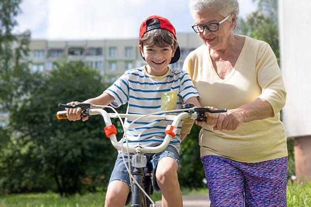 istock Smiling Elderly Woman Teaching Boy to Ride Bicycle Outdoors in Summer. Copyspace 2226360241