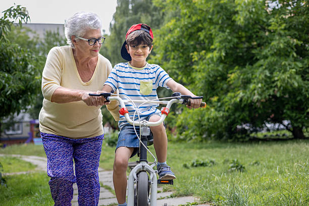 istock Smiling Elderly Woman Teaching Boy to Ride Bicycle Outdoors in Summer. Copyspace 2226360373