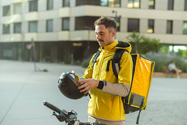 istock Bicycle delivery courier preparing helmet in urban setting wearing bright yellow backpack 2226364580