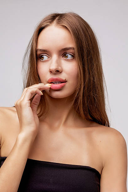Young woman poses naturally with gentle expression in studio setting, showcasing long hair and casual elegance