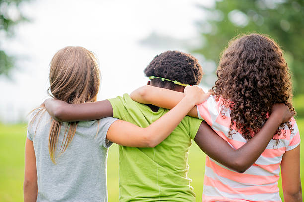 Three children sitting outdoors, embracing each other in solidarity and connection. Bonds, care, and diversity emphasized in the natural backdrop.