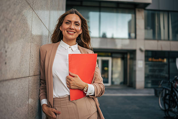 istock Smiling businesswoman leaning against wall holding red folder 2226374923