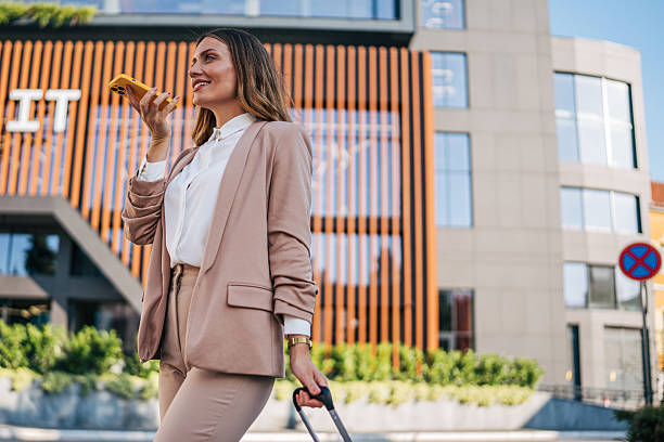 istock Businesswoman using smartphone while pulling suitcase in front of modern office building 2226375825